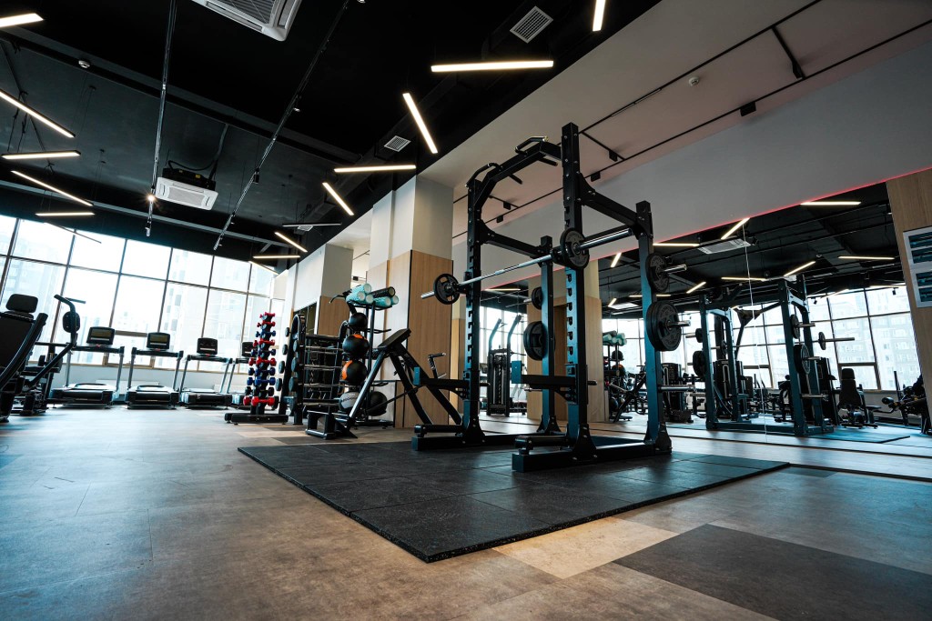 Assorted fitness equipment including dumbbells, kettlebells, resistance bands, and a weight bench in a modern gym